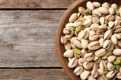 Photo of Organic pistachio nuts in bowl on wooden table, top view. Space for text