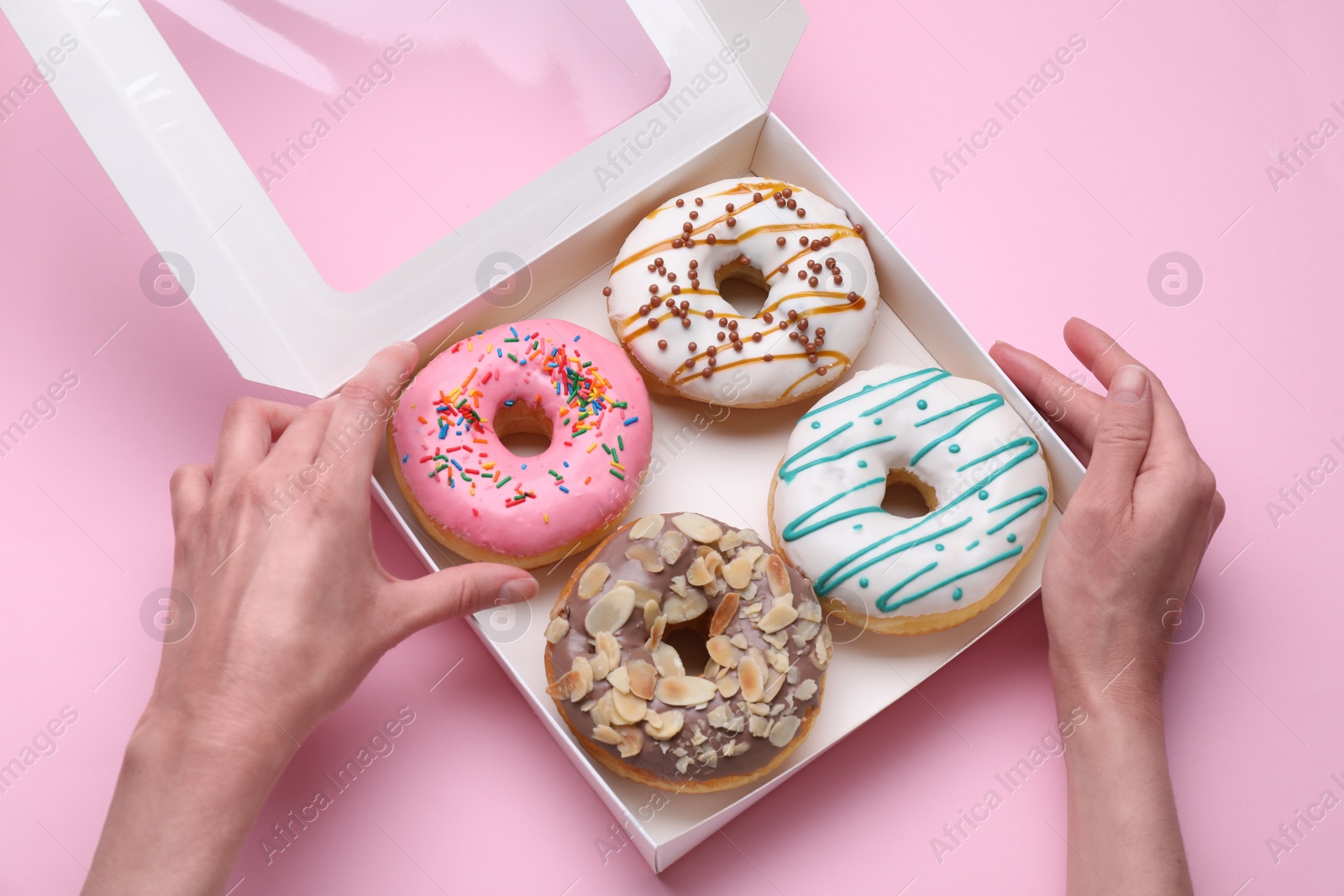 Photo of Woman taking tasty glazed donut from box on pink background, top view