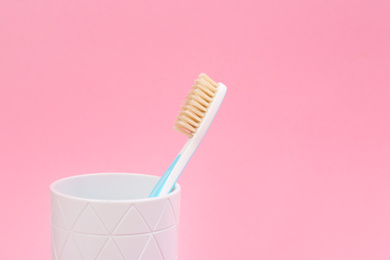 Photo of Natural bristle toothbrush in holder on pink background. Space for text