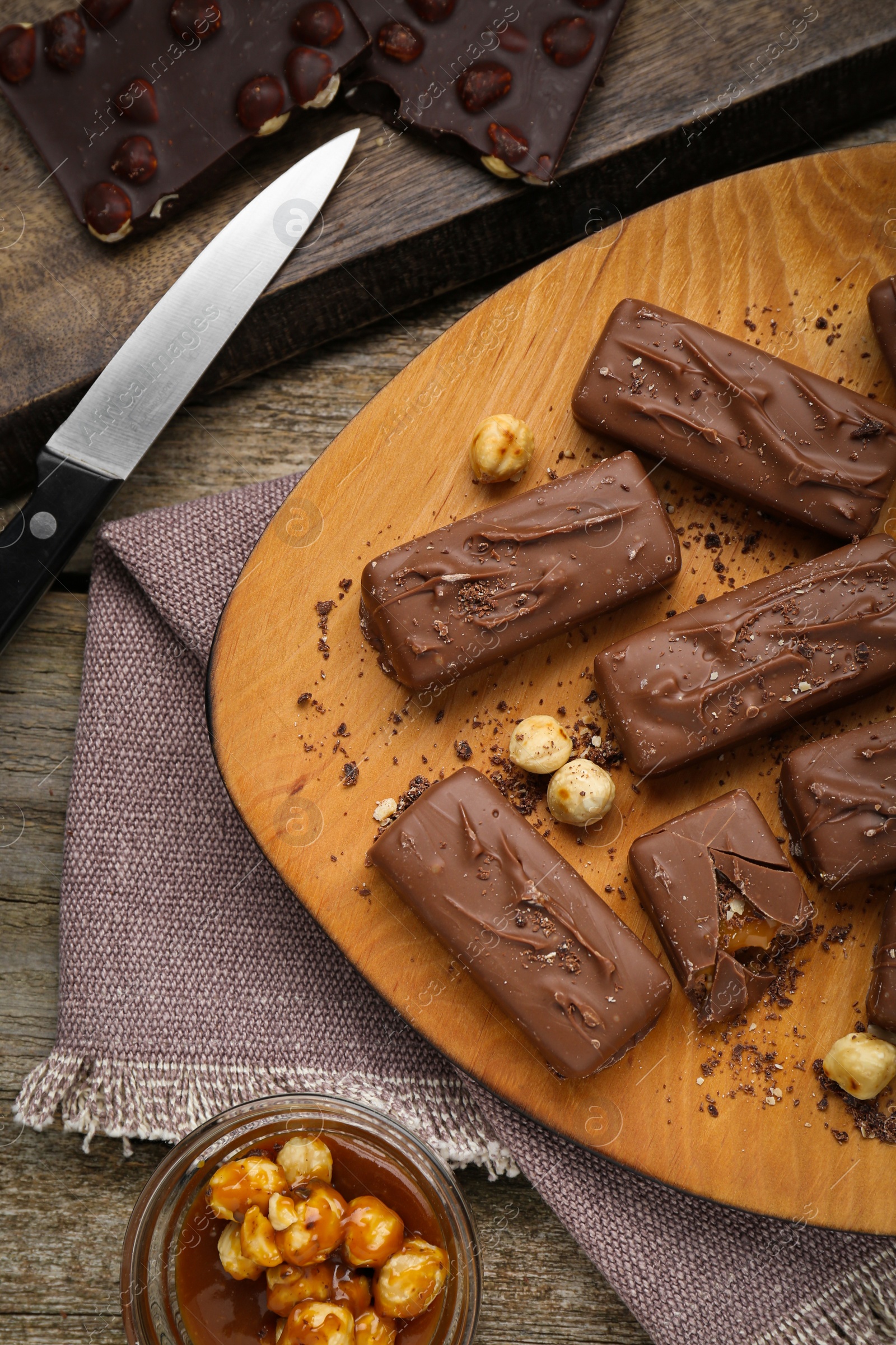 Photo of Delicious chocolate candy bars with caramel and nuts on wooden table, flat lay