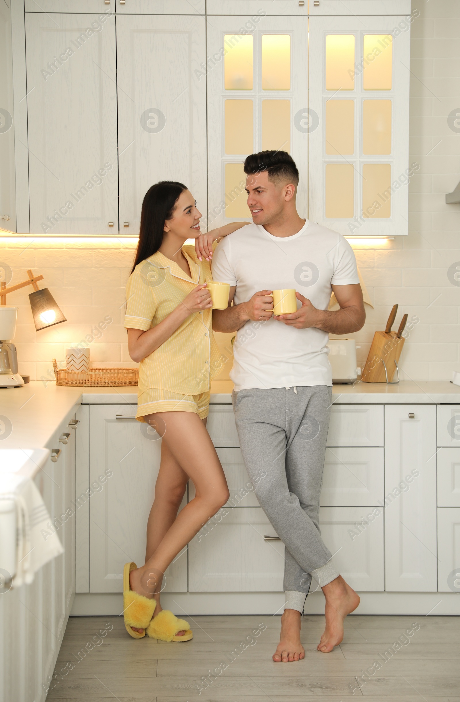 Photo of Happy couple wearing pyjamas with cups of coffee in kitchen