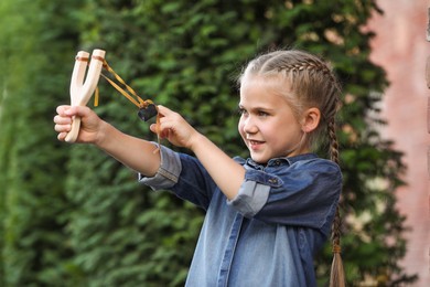 Photo of Little girl playing with slingshot outdoors. Kid's toy