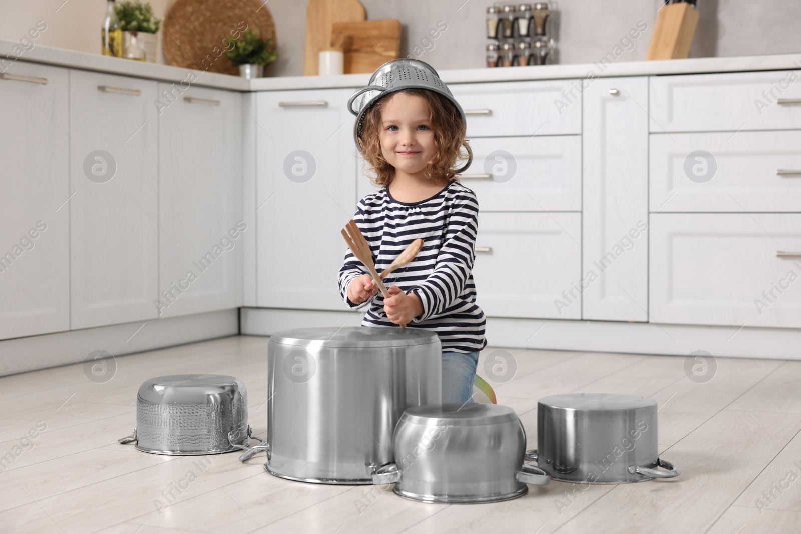 Photo of Little girl pretending to play drums on pots in kitchen