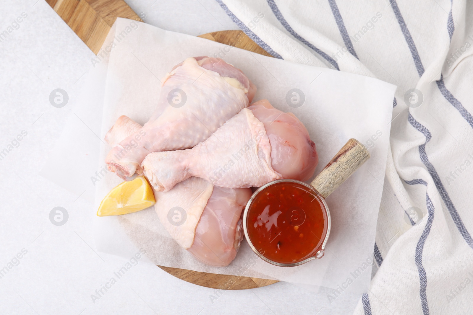 Photo of Fresh marinade, raw chicken drumsticks and lemon wedge on light table, top view