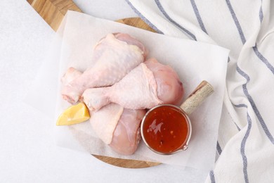 Fresh marinade, raw chicken drumsticks and lemon wedge on light table, top view