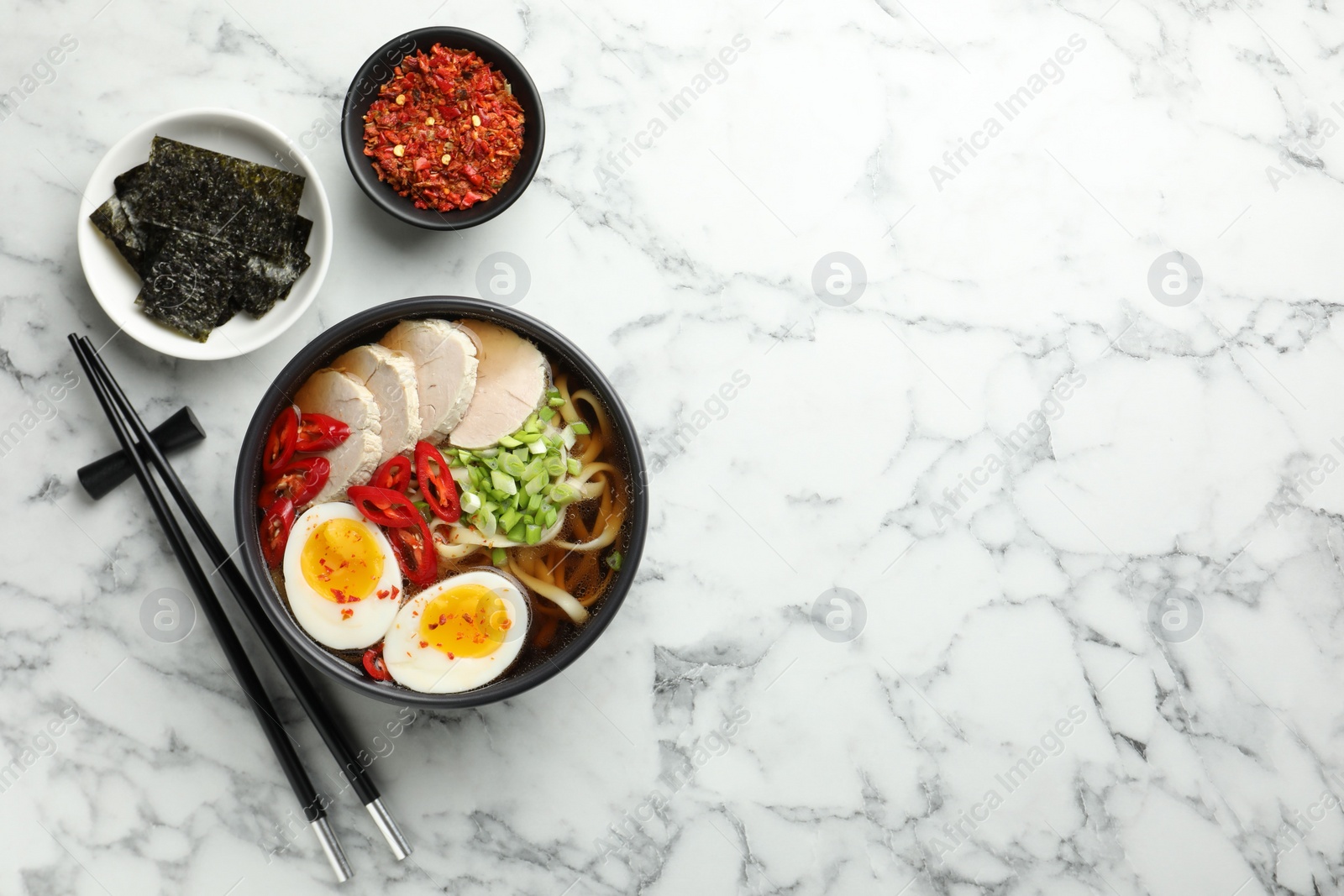 Photo of Delicious ramen in bowl served on white marble table, flat lay with space for text. Noodle soup