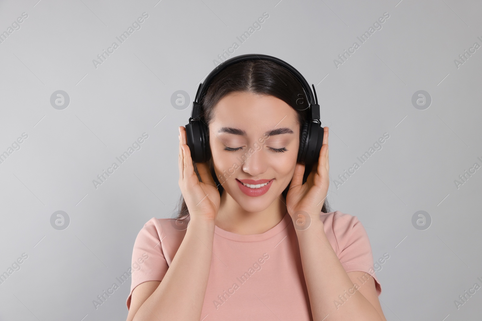 Photo of Happy woman in headphones enjoying music on grey background
