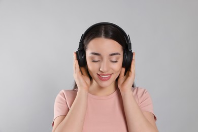 Happy woman in headphones enjoying music on grey background