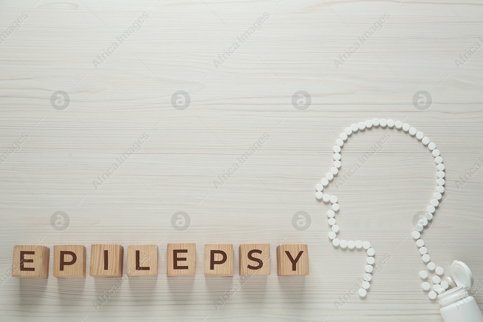 Photo of Wooden cubes with word Epilepsy and human head silhouette made of pills on white table, flat lay. Space for text