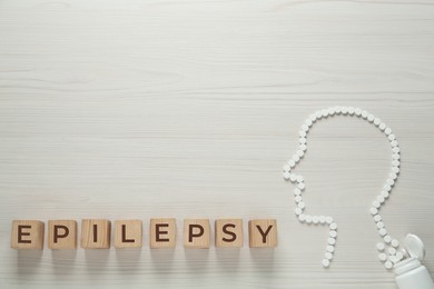 Photo of Wooden cubes with word Epilepsy and human head silhouette made of pills on white table, flat lay. Space for text
