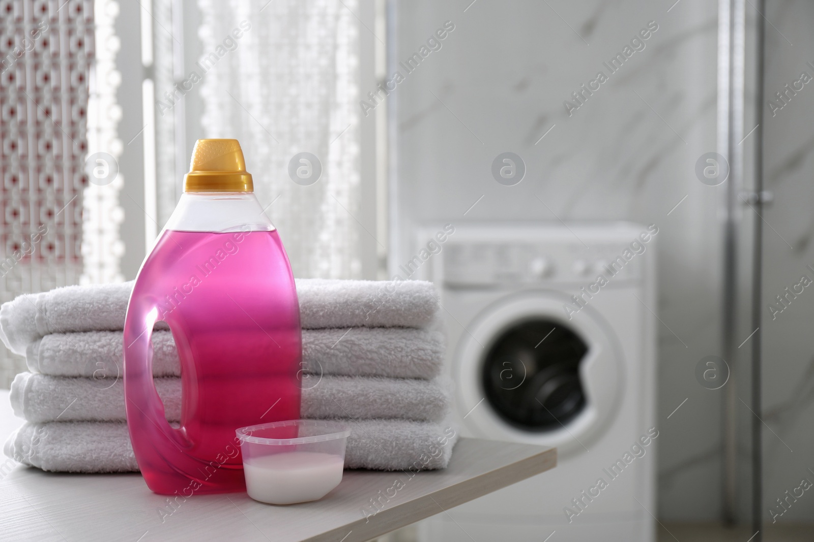 Photo of Stack of folded towels and detergents on white table in bathroom, space for text