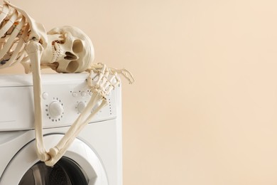 Photo of Waiting concept. Human skeleton lying on washing machine near beige wall indoors, space for text