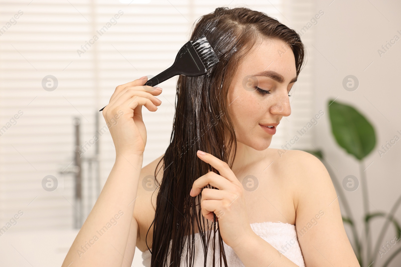 Photo of Young woman applying hair mask in bathroom