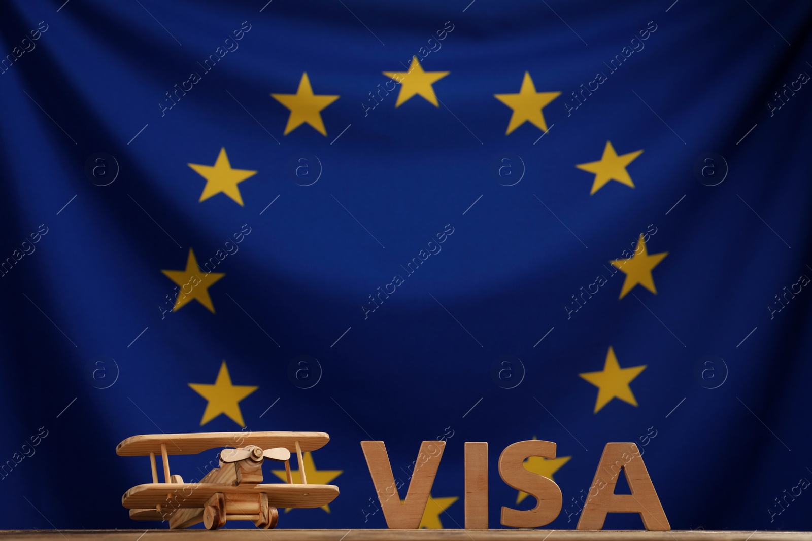 Photo of Word Visa made of wooden letters and toy plane on table against European Union flag. Space for text