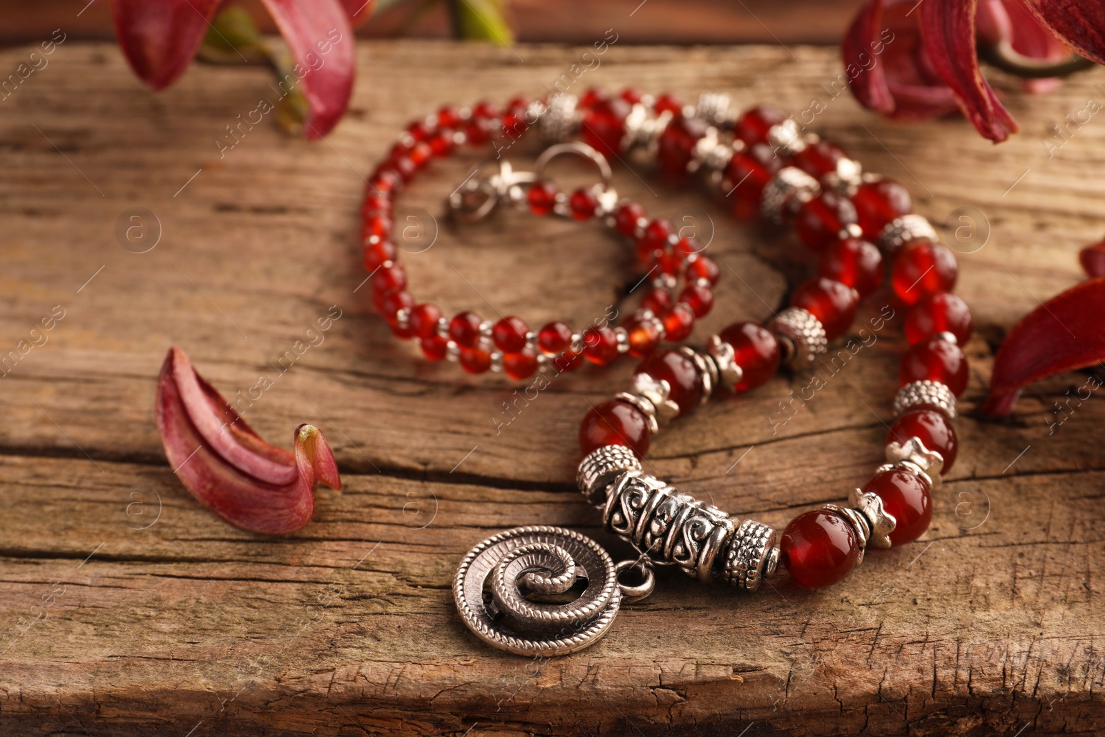 Photo of Beautiful necklace with gemstones and lily flowers on wooden surface, closeup