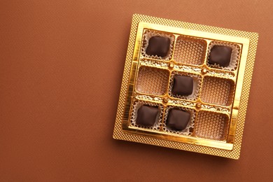 Partially empty box of chocolate candies on brown background, top view. Space for text