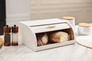 Wooden bread basket with freshly baked loaves on white marble table in kitchen