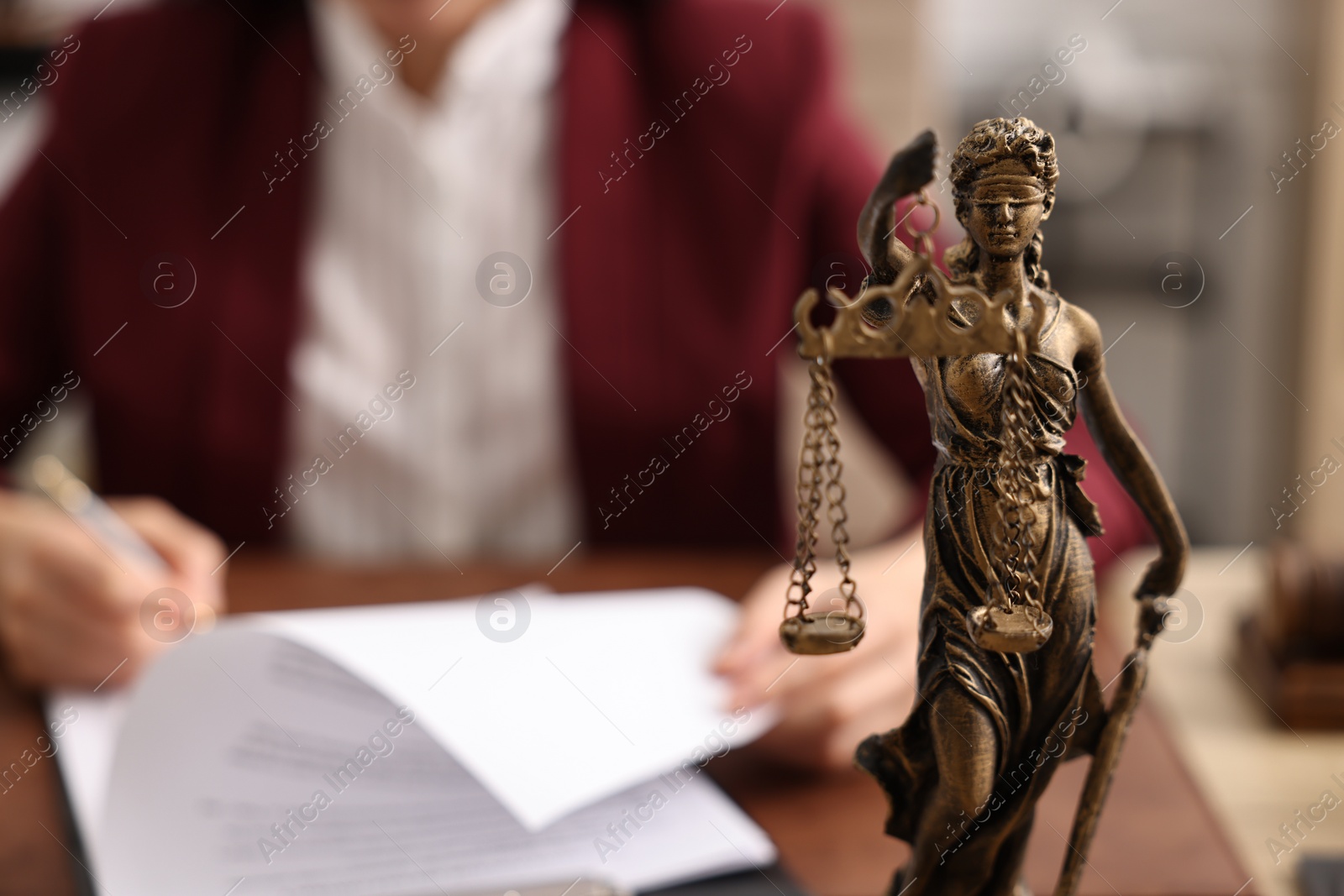 Photo of Notary signing document at table in office, focus on statue of Lady Justice