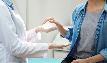 Doctor showing silicone implants for breast augmentation to patient in clinic, closeup. Cosmetic surgery