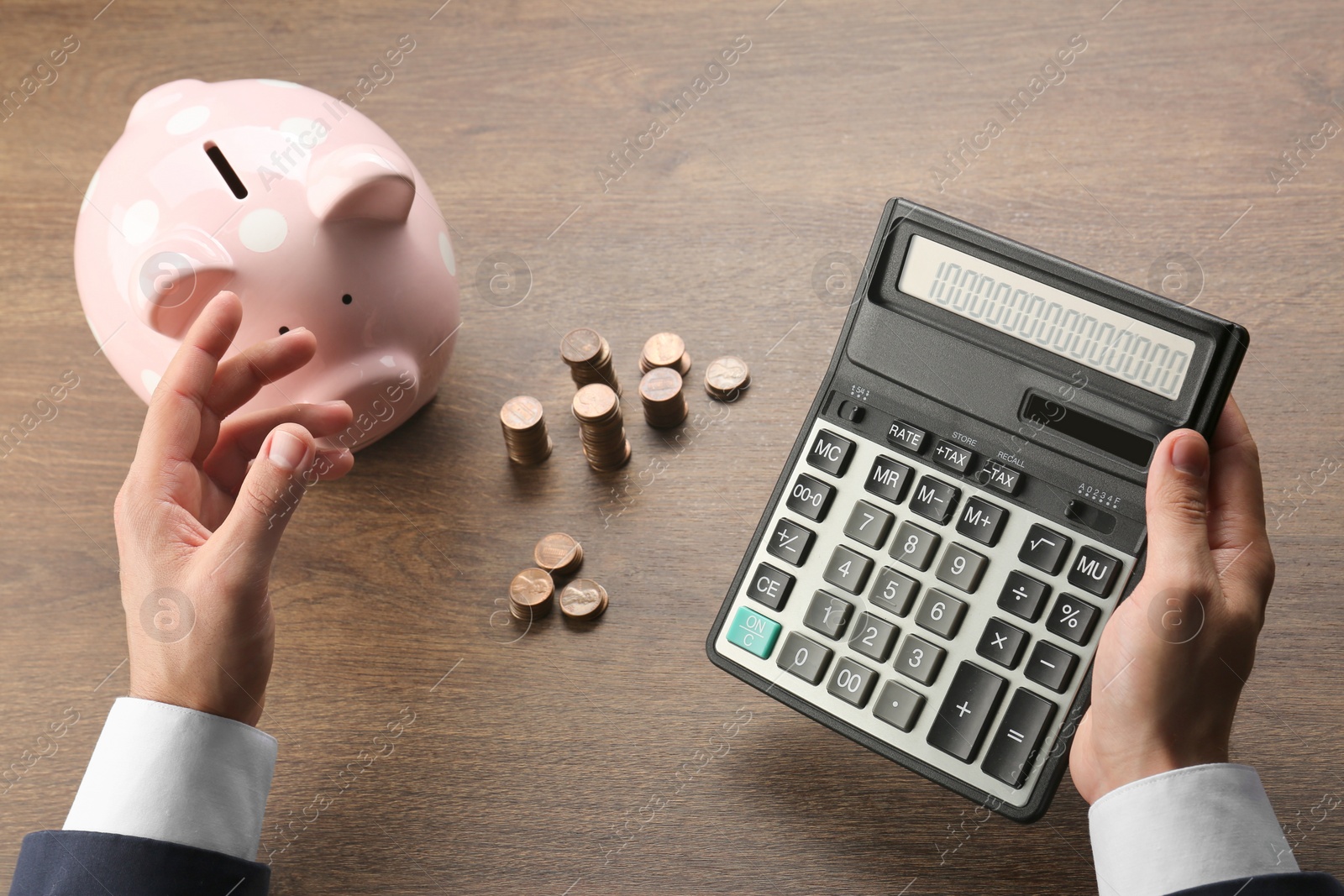 Photo of Budget planning. Businessman calculating with piggy bank at wooden table, closeup