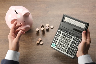 Budget planning. Businessman calculating with piggy bank at wooden table, closeup