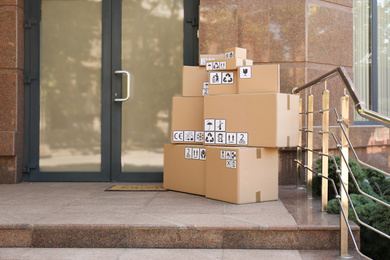 Photo of Cardboard boxes with different packaging symbols on porch near entrance, space for text. Parcel delivery