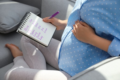Photo of Pregnant woman with baby names list sitting on sofa, closeup