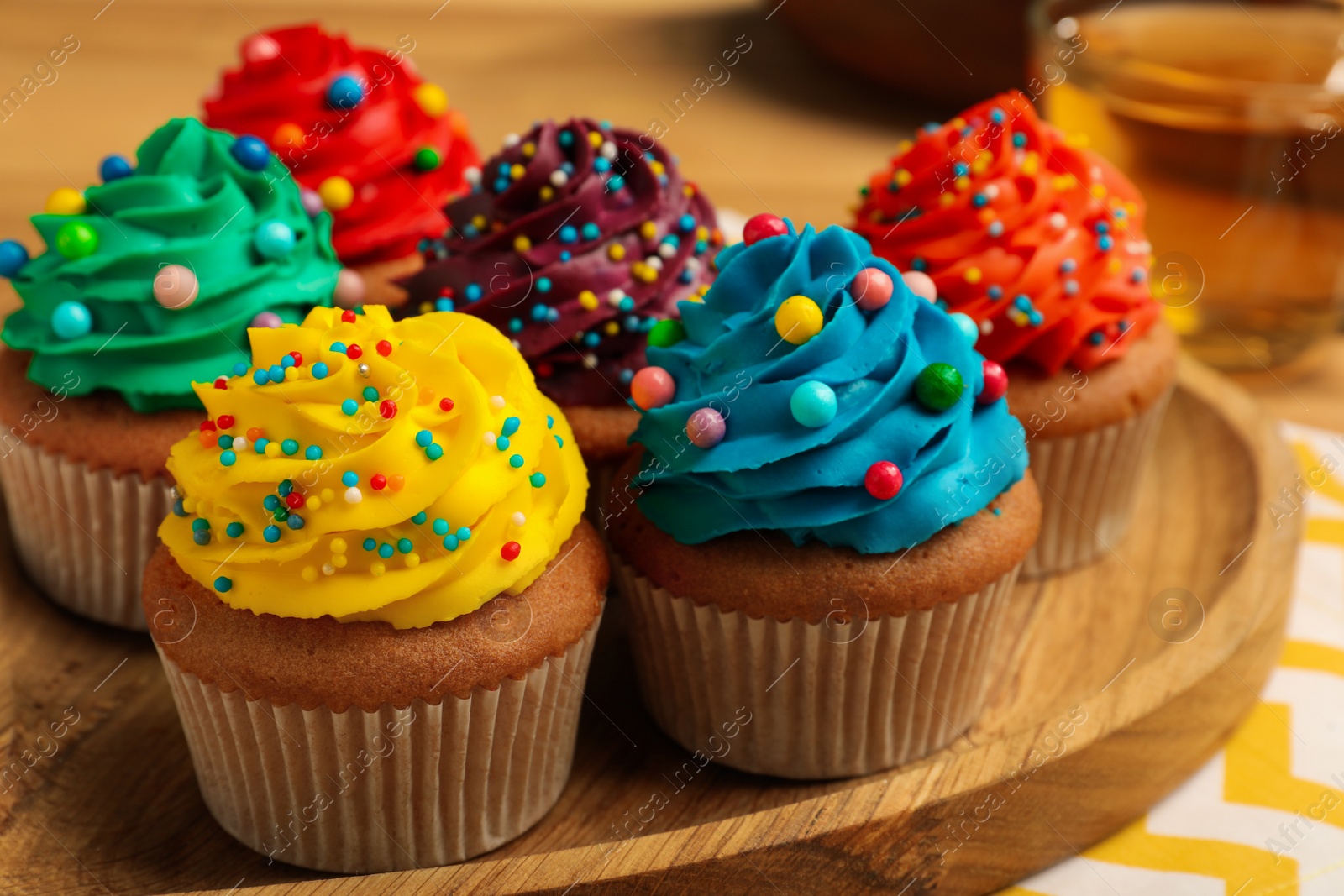 Photo of Delicious cupcakes with colorful cream and sprinkles on wooden board, closeup