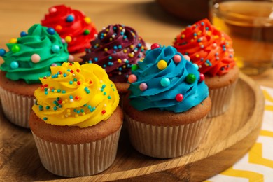 Delicious cupcakes with colorful cream and sprinkles on wooden board, closeup