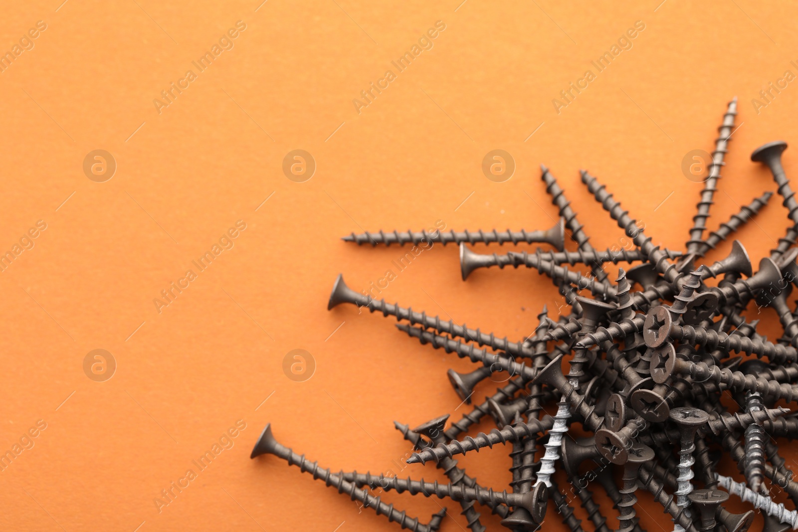 Photo of Many metal screws on orange background, top view. Space for text