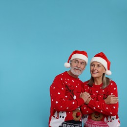 Photo of Senior couple in Christmas sweaters and Santa hats on light blue background. Space for text