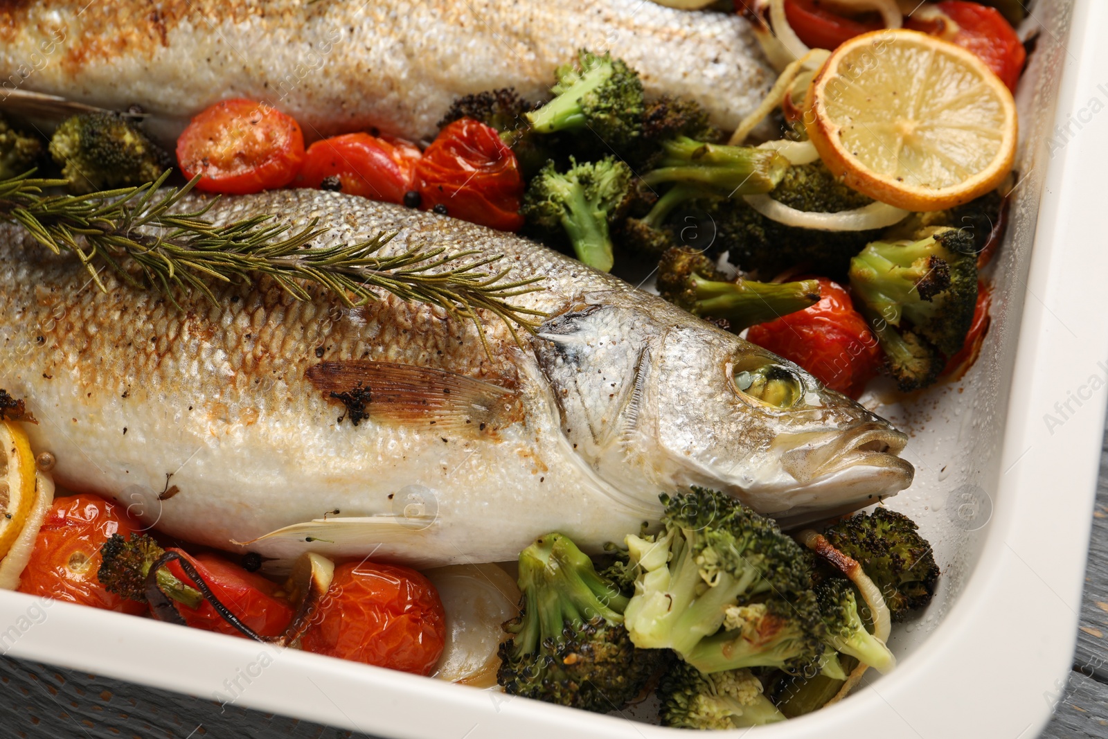 Photo of Delicious fish with vegetables and lemon in baking dish on table, closeup