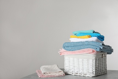 Wicker laundry basket with clean towels on table against light background. Space for text