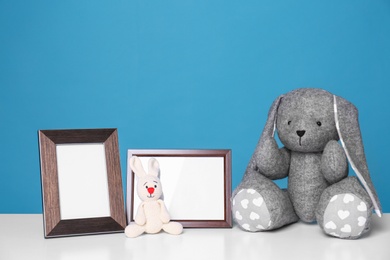Photo of Photo frames and adorable toy bunnies on table against color background, space for text. Child room elements