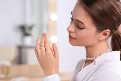 Photo of Young woman trying on elegant ring with pearls indoors, closeup. Space for text