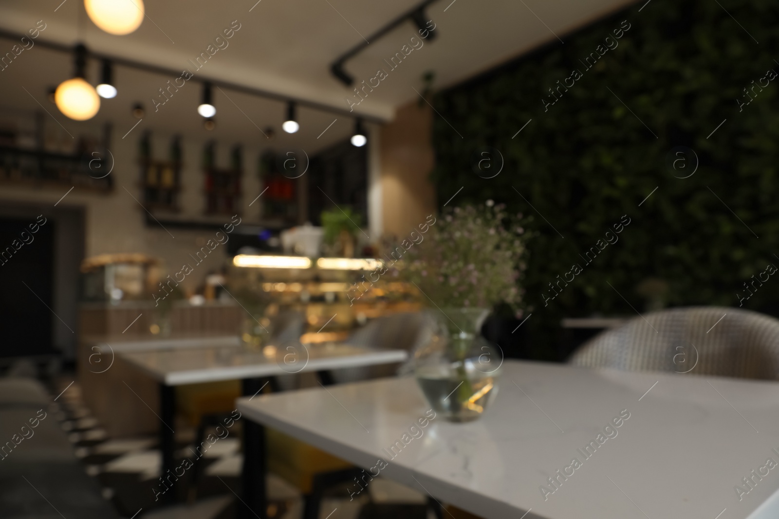 Photo of Glass vase with bouquet of beautiful flowers on table in cafe, blurred view