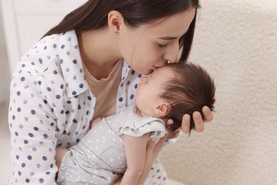 Photo of Mother kissing her sleeping newborn baby indoors
