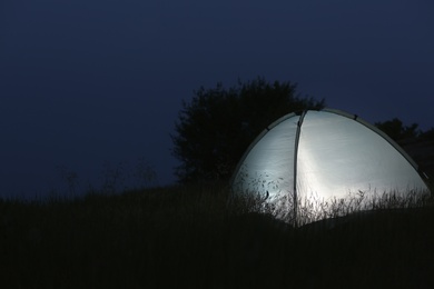 Modern tent lit from inside in wilderness at night, space for text. Overnight camping