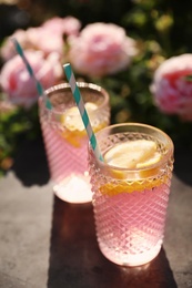 Photo of Glasses of pink rose lemonade on table in blooming garden