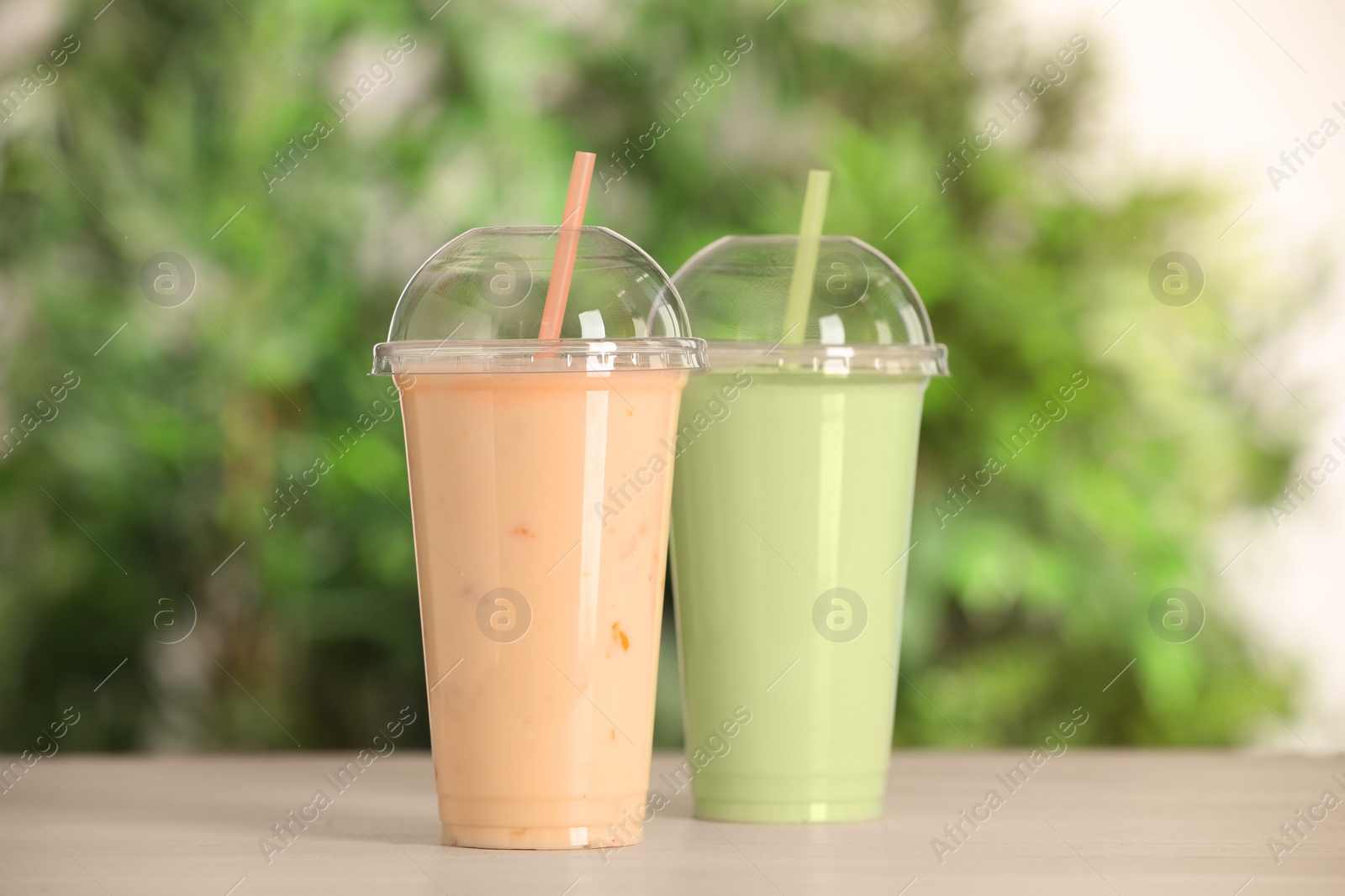 Photo of Plastic cups with different tasty smoothies on wooden table outdoors