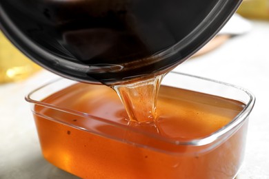 Photo of Pouring used cooking oil from saucepan into container on beige table, closeup