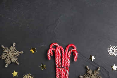 Sweet candy canes and Christmas decor on black background, flat lay. Space for text