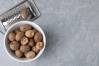 Photo of Nutmegs in bowl and metal grater on light grey table, flat lay. Space for text