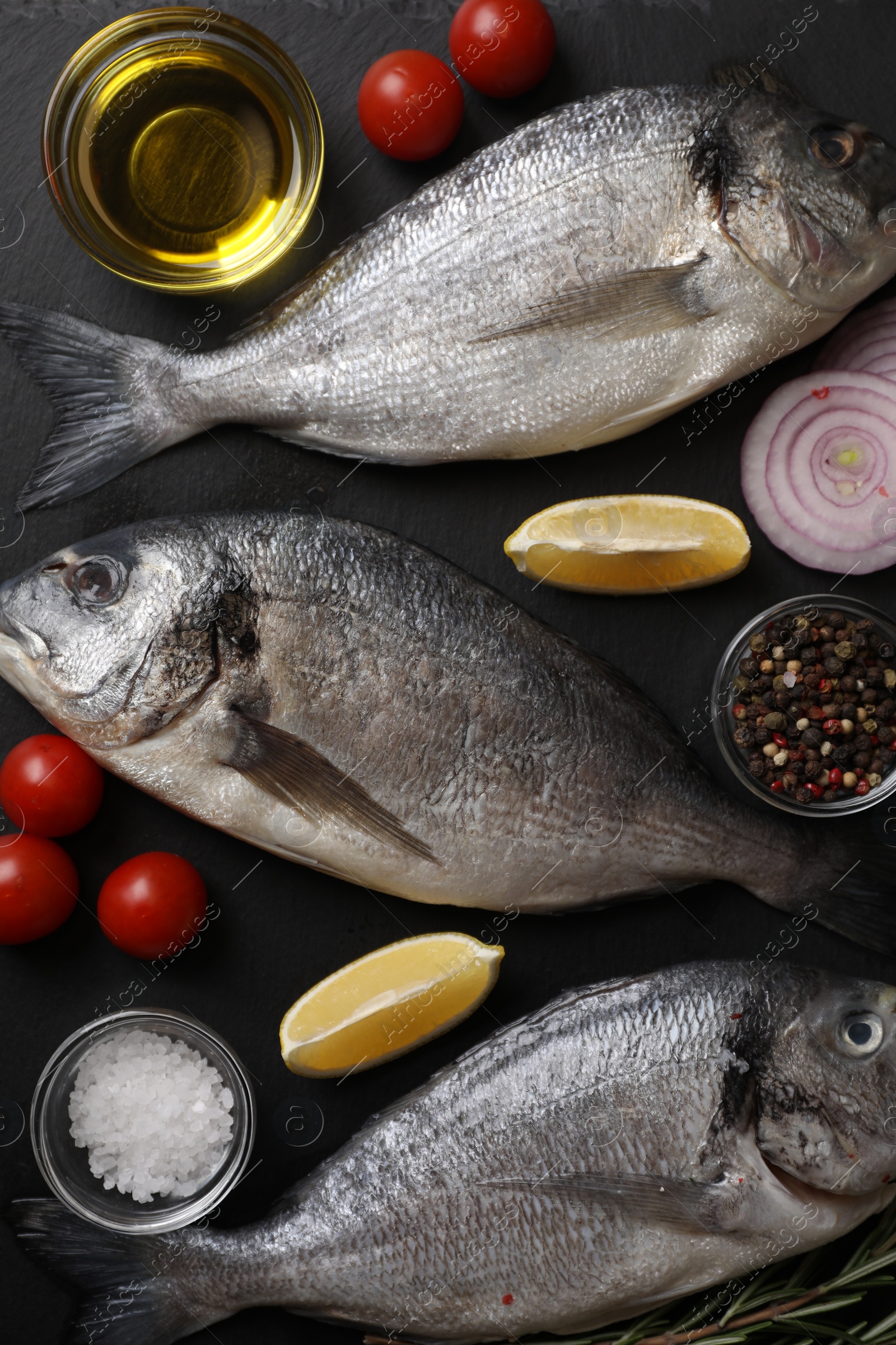 Photo of Fresh raw dorado fish, lemon wedges, spices and tomatoes on black table, flat lay