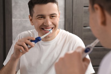 Man brushing his teeth with electric toothbrush near mirror in bathroom