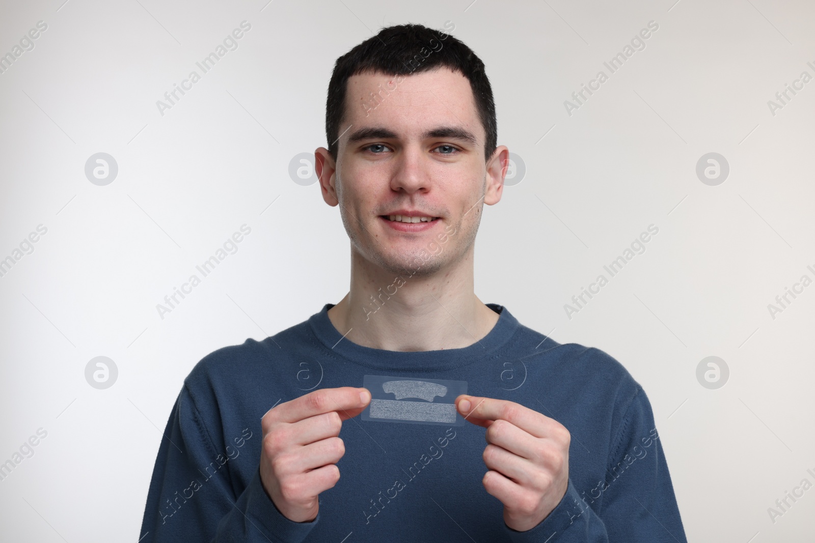 Photo of Young man with whitening strips on light background