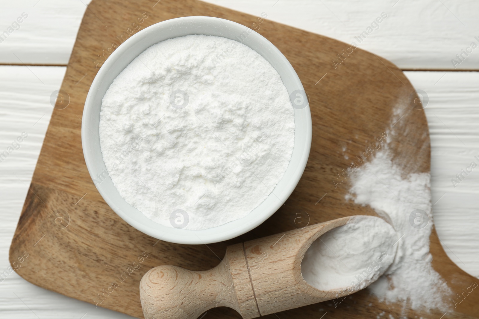 Photo of Baking powder in bowl and scoop on white wooden table, top view