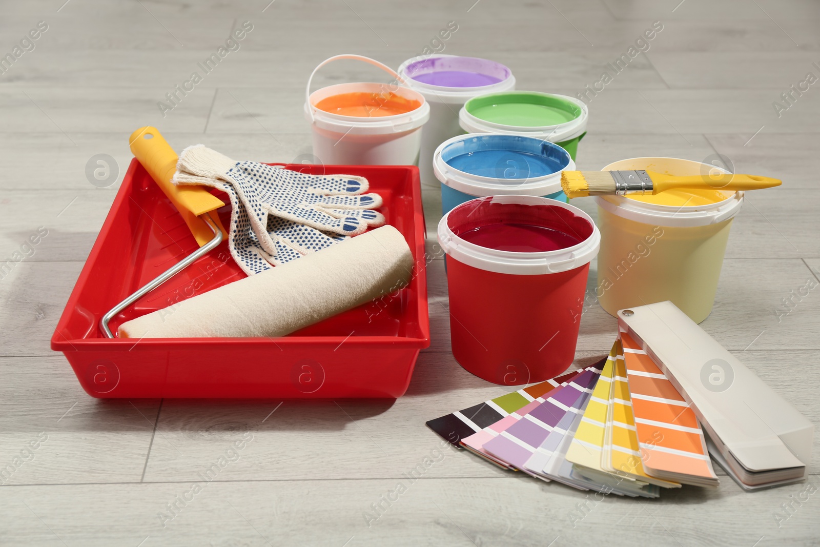 Photo of Buckets of paints, palette and decorator's tools on light wooden background