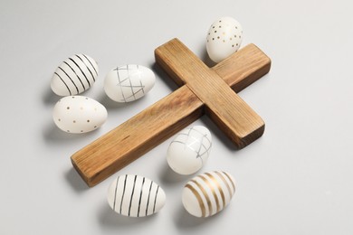 Wooden cross and painted Easter eggs on light grey background