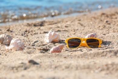 Photo of Sunglasses and shells on sand near sea. Beach object